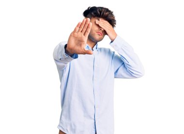 Elleriyle gözlerini kapatan ve üzgün ve korku ifadeleriyle jest yapan İspanyol asıllı genç bir adam. utangaç ve olumsuz kavram. 