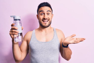 Sakallı genç yakışıklı sporcu kolsuz tişört giyiyor. Bir şişe su içiyor, başarıyı kutluyor. Gülümsüyor ve el kaldırıyor.