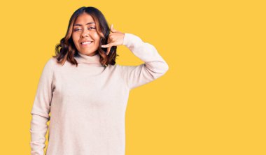 Balıkçı yaka kazak giyen, gülümseyen, el ve parmaklarıyla telefonla konuşan güzel, melez bir kadın. iletişim kavramları. 