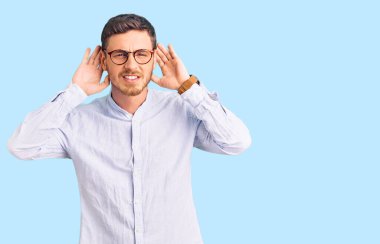 Zarif iş gömleği ve gözlük takan yakışıklı genç adam iki elini de kulak hareketi yaparken duymaya çalışıyor, dedikoduya meraklı. İşitme sorunu, sağır 