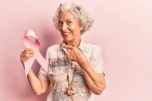 シニア白髪の女性保持ピンク癌リボン笑顔幸せなポインティングとともに手と指 — ストック写真