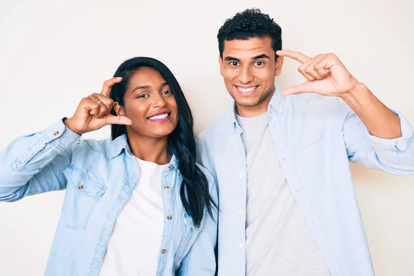 Beautiful latin young couple wearing casual clothes smiling and confident gesturing with hand doing small size sign with fingers looking and the camera. measure concept.