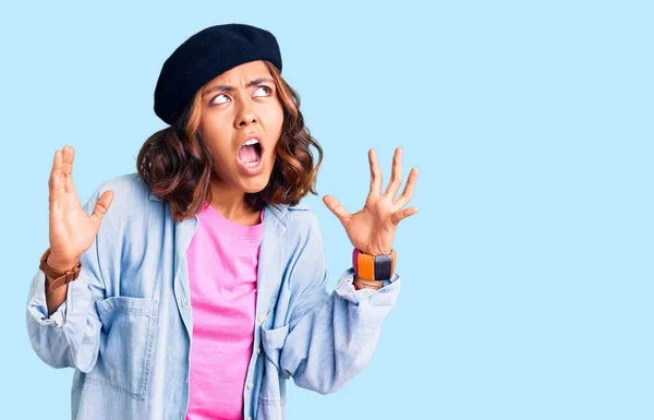 Young beautiful mixed race woman wearing french look with beret crazy and mad shouting and yelling with aggressive expression and arms raised. frustration concept.