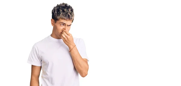 若いハンサムな男は 鼻の上に指で息を保持し 臭いと嫌な 耐え難い臭い何かを嗅ぐカジュアルな白いTシャツを着て 臭いが悪い — ストック写真