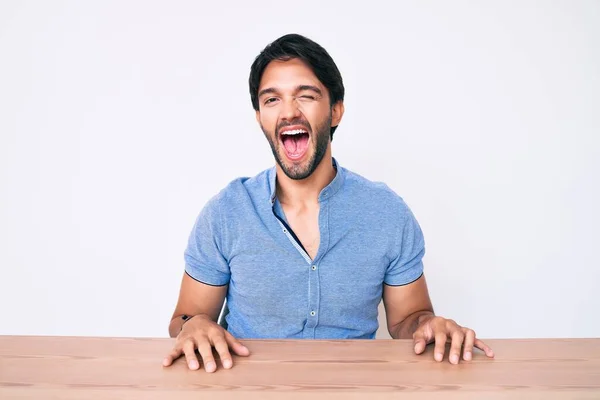 Bonito Homem Hispânico Vestindo Roupas Casuais Sentado Mesa Piscando Olhando — Fotografia de Stock