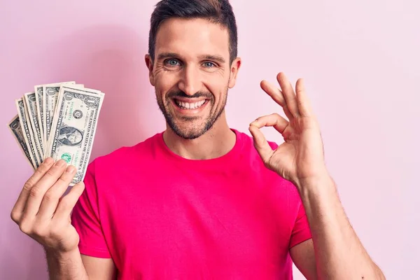 잘생긴 남자가 분홍색 지폐를 손가락으로 괜찮은 사인을 다정하게 미소를 있습니다 — 스톡 사진