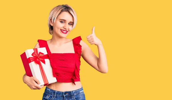 Young Beautiful Blonde Woman Holding Gift Smiling Happy Positive Thumb — Stock Photo, Image