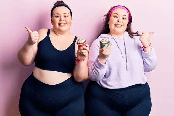 Young Size Twins Wearing Sportswear Holding Cupcake Pointing Thumb Side — Stock Photo, Image