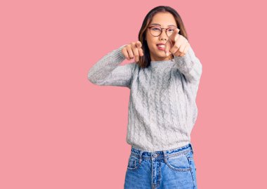 Genç, güzel Çinli kız, günlük giysiler içinde seni ve kamerayı işaret ediyor, gülümsüyor, pozitif ve neşeli 