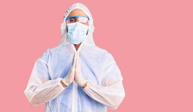 Koronavirüs üniforması ve tıbbi maske takan genç İspanyol adam ellerini birleştirip af diliyor kendinden emin bir şekilde gülümseyerek.. 