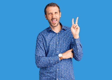 Sıradan kıyafetler giyen, gülen, kameraya göz kırpan, zafer işareti yapan genç yakışıklı bir adam. İki numara.. 