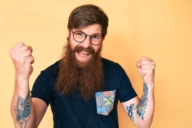 Uzun sakallı, sıradan kıyafetler ve gözlüklü yakışıklı genç adam gururla bağırıyor, zaferi kutluyor ve başarıyı kollarını kaldırarak kutluyor. 