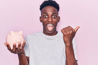 Genç Afrikalı Amerikalı domuz kumbarası tutan ve ağzı açık gülümseyen bir adam. 