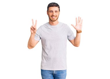 Ayılı yakışıklı genç adam gündelik tişört giyer ve yedi numaralı parmaklarını göstererek gülümserken kendinden emin ve mutlu.. 