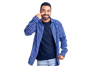 Latin asıllı genç bir adam, gündelik giysiler giyip el ve burnu işaret ediyor, neşeli bir şekilde gülümsüyor. güzellik konsepti 
