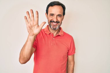 Orta yaşlı İspanyol bir adam, günlük kıyafetler giyip beş numarayı gösterip işaret ederken kendinden emin ve mutlu bir şekilde gülümsüyor.. 