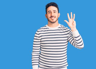İspanyol asıllı genç adam, gündelik giysiler giyip dört numarayı gösterip işaret ederken kendinden emin ve mutlu bir şekilde gülümsüyor.. 