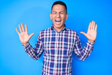 Gündelik giysiler giyen genç, yakışıklı, çılgın ve başarıyı kutlayan, kollarını kaldırmış, gözlerini kapatmış heyecanlı çığlıklar atan Latin bir adam. Kazanan konsept 