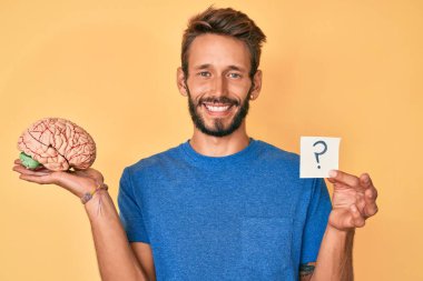 Sakallı, sakallı ve soru işaretiyle gülümseyen yakışıklı, beyaz bir adam. diş gösterme. 