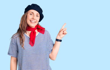 Fransız beresi ve çizgili tişört giyen, yüzünde kocaman bir gülümseme olan genç, güzel sarışın kadın kameraya el ile işaret ediyor.. 