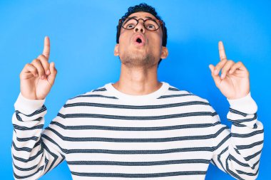 Gündelik süveter giyen ve gözlüklü genç, yakışıklı İspanyol adam şaşırmış ve şaşırmış bir şekilde yukarı baktı ve parmaklarıyla işaret ederek kollarını kaldırdı.. 