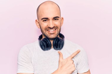 Genç yakışıklı kel adam kulaklıkla müzik dinliyor. Gülümsüyor, elleri ve parmakları yana bakıyor. 