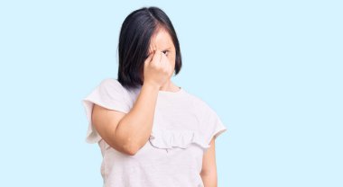 Down sendromlu esmer bir kadın günlük beyaz tişört giyiyor. Burnu ve gözleri ovuşturup yorgun ve baş ağrısı çekiyor. Stres ve hüsran kavramı. 