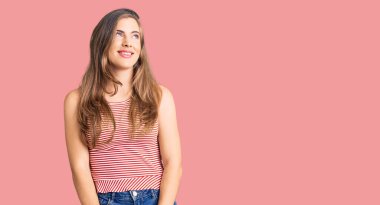 Güzel, beyaz, sıradan kıyafetler giyen, yüzünde gülümseme ve doğal bir ifadeyle yan yana bakan bir kadın. Kendinden emin gülen. 