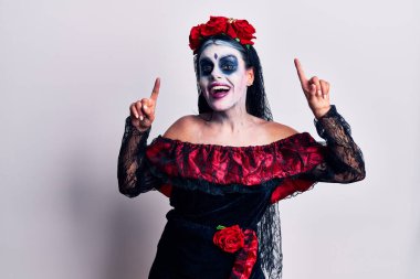 Meksika makyajlı genç bir kadın. Gülümsüyor, şaşırıyor ve parmaklarıyla işaret ediyor ve kollarını kaldırıyor.. 