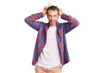 Genç, yakışıklı, günlük kıyafetler giyen, komik ve çılgın poz veren, parmakları tavşan kulaklı, neşeli gülümseyen bir adam. 