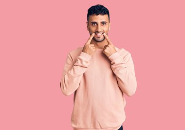 Gündelik kıyafetler giymiş, ağzı açık gülümseyen, parmakları işaret eden ve neşeli gülümsemeye zorlayan genç İspanyol bir adam. 