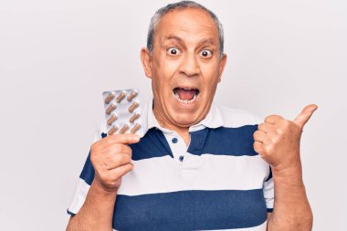 Yaşlı adam elinde haplarla baş parmağını kaldırmış ağzı açık gülümsüyor. 