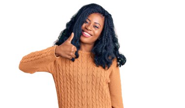 Güzel afro-amerikan kadın gündelik süveter giyip mutlu bir el hareketi yapıyor. Kameraya bakıp başarıyı gösteren ifade. 