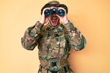 Genç beyaz adam kamuflaj üniforması giyiyor kızgın ve kızgın dürbünler kullanıyor ve öfkeyle bağırıyor öfkeyle bağırıyor. öfke ve agresif konsept. 