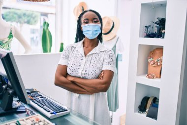 Giyim mağazasında çalışan, tıbbi maske takan Afro-Amerikan bir kadın.