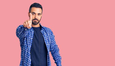 Latin asıllı genç bir adam, gündelik giysiler giyip parmağını kaldırmış ve kızgın bir ifade takınıyor. 