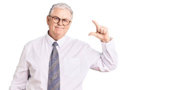 İş kıyafetleri giymiş, gülümseyen, kendine güvenen, el hareketi yapan, parmaklarıyla işaret yapan, kameraya bakan yaşlı gri saçlı bir adam. ölçüm kavramı. 