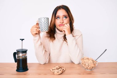 Genç, güzel, beyaz bir kadın kahvaltı yapıyor. Ciddi bir yüz ifadesi takınıyor. Soruları sorup duruyor. 