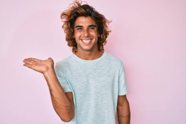 Gündelik kıyafetler giyen genç İspanyol adam neşeli bir şekilde gülümsüyor ve avuç içi kameraya bakıyor.. 