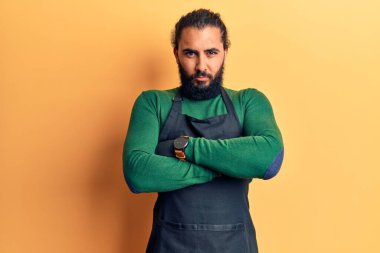 Genç Arap adam berber önlüğü takıyor şüpheci ve gergin, yüzünde çapraz kollu tasvip etmeyen bir ifade. negatif kişi. 