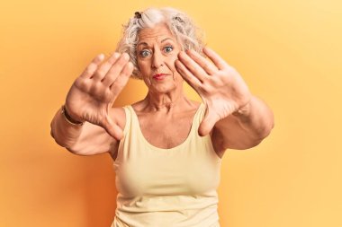 Kıdemli, gri saçlı, günlük kıyafetler giyen, el ve parmaklarını kullanarak çerçeve yapan, kamera perspektifi olan kadın. 