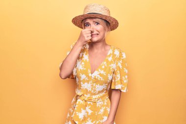 Yaz şapkası takmış, sarı arka planda giyinmiş güzel sarışın kadın pis ve iğrenç bir koku alıyor, nefes nefese kalmış, parmakları burnunda. Kötü kokuyor.