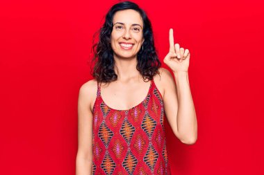 Genç ve güzel İspanyol bir kadın gündelik kıyafetler giyip gülümsüyor bir fikir veya soru işareti ile mutlu bir yüzle, bir numara 