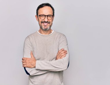 İzole edilmiş beyaz arka planda gözlüklü, sıradan bir süveter giyen, kollarını kavuşturup kameraya gülümseyen orta yaşlı yakışıklı bir adam. Pozitif kişi.