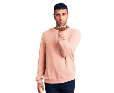 Gündelik giysiler giymiş genç İspanyol bir adam kameraya bakıp havada bir öpücük savuruyor ve sevimli ve seksi oluyor. aşk ifadesi. 