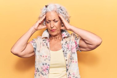 Yaşlı, gri saçlı, günlük kıyafetler giyen, baş ağrısı çeken çaresiz ve stresli bir kadın. Çünkü acı ve migren ağrısı var. Eller başının üstünde.. 