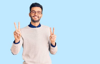 Zarif kıyafetler ve gözlük takan yakışıklı İspanyol adam kameraya bakıp zafer işareti yapıyor. İki numara.. 