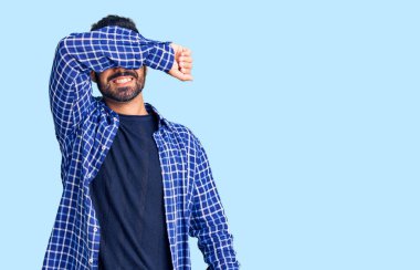 Genç İspanyol adam günlük kıyafetler giyip kollarıyla gözlerini kapatıyor neşeli ve komik gülümsüyor. kör kavram. 