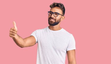 Gündelik kıyafetler ve gözlük takan genç İspanyol adam gururlu görünüyor, gülümsüyor yan tarafa baş parmak hareketi yapıyor. 