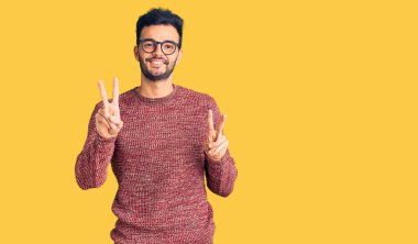 Kışlık süveter giyen, gülümseyen ve parmaklarını zafer işareti yaparken gösteren genç, yakışıklı İspanyol adam. İki numara.. 